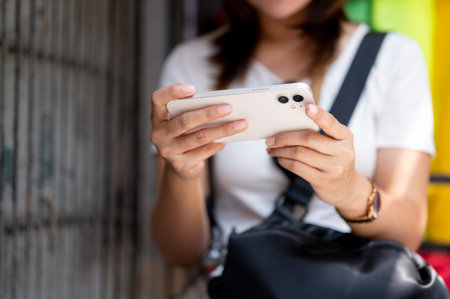 Close up of asian tourist woman holding phone in both hands standing in front of the shop in local market. Tourist spot, Walking street, Old town trip.の写真素材