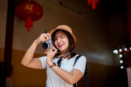 Asian woman wearing hat smiling while holding a camera taking photos inside the Chinese shrine temple. Tourist spot, Blessing place, Historical place.の写真素材