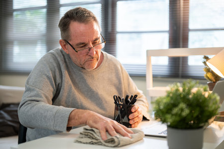 Old white caucasian man hand holding a cloth rag cleaning or wiping the dust off white working table in his room. Housework, household chores.の写真素材