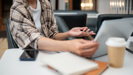Close up of a man hands touching on laptop lid or screen with phone and notebook aside sitting at white table in cafe. Study or Working, Going Outside.の写真素材