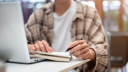 Close up of a man hands writing in notebook with a fountain pen over a laptop while sitting at white table in cafe. Study or Working, Going Outside.の写真素材
