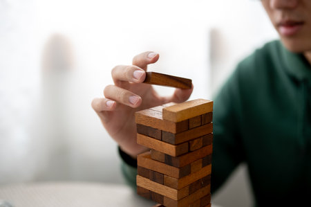 Close up man's hand putting a piece on top of wooden blocks in tower building game as playing alone....
