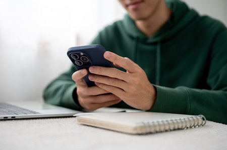 Close up a man holding phone with both hands aside notebook and laptop at table in a cafe or...