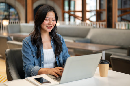 Asian woman student looking typing on laptop with phone and notebook on table in cafe or coffee shop. Working or Study, Freelancer, Urban City Life.の写真素材