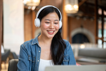 Happy asian woman wearing headphones looking at laptop watching video or movie at table in the cafe. Entertainment, Leisure Time, Urban City Life.の写真素材