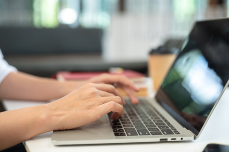 Close up of a woman student's hands typing on laptop aside coffee cup while sitting at table in cafe. Freelancer, Working or Study, Modern Urban Life.の写真素材