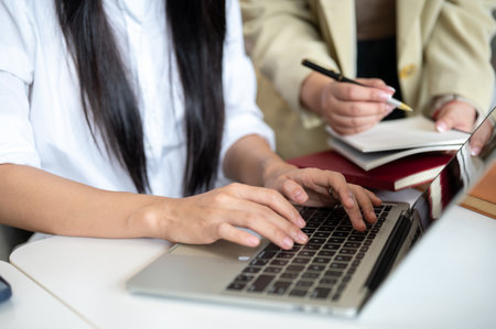 Close up of a woman student's hands on laptop with teacher holding pen checking her work at table. Thesis, Working or Study, Modern Urban Life.の写真素材