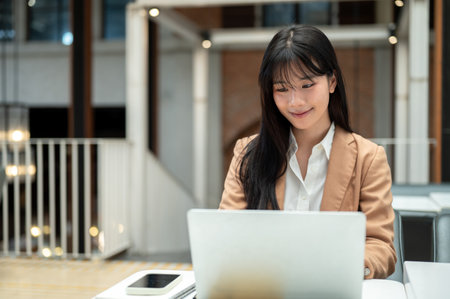 Businesswoman or office worker looking using laptop aside phone and notebook on table in cafe. Professional Suit, Remote Working, Daily Life.の写真素材
