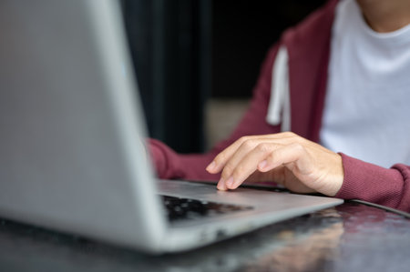 Close up of a man student's hand typing or tapping on laptop at shiny black table in cafe or...