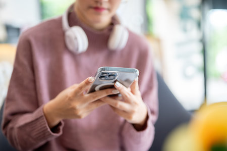 Close up of a young woman looking at phone holding with both hands while sitting on sofa in a cafe. Leisure Free Time, Urban Life.の写真素材