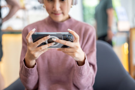 Close up of young woman holding phone in horizontal with both hands while sitting on sofa in a cafe....