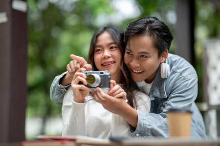 Young asian couple a man teaching a woman taking photos on camera sitting at outdoor table in cafe. Dating activity, Urban Life, Chilling Outdoorsの写真素材