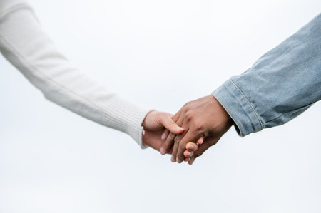 Close up of a young couple holding hands standing outdoors under bright sky or white background....