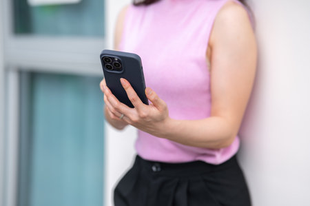 Close up of a woman's hands holding and using smartphone while standing or leaning against the wall. Urban Life, Chilling Outdoors.の写真素材