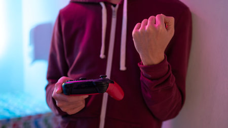 Close up man hand holding game console controller making a fist in excited after winning in dim...