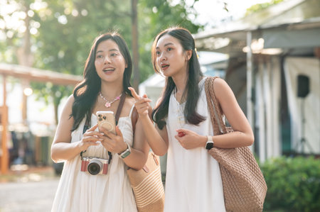 Pretty asian woman holding phone aside a friend talking pointing while standing in the local market. Travel Trip, Tourist destination, Holiday Vacation.の写真素材