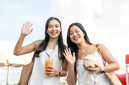 Pretty asian woman with juice drink cup waving a hand with friend holding coconut in local market. Travel Trip, Tourist destination, Holiday Vacation.の写真素材