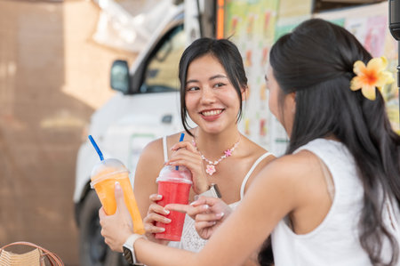 Pretty asian woman holding fresh juice enjoy drinking with a friend while sitting aside food truck....