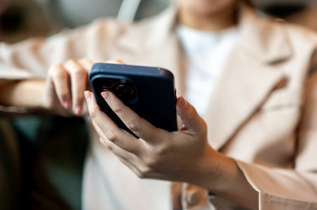 Close up woman holding and touching on smartphone while sitting putting elbow on green sofa in cafe.の写真素材
