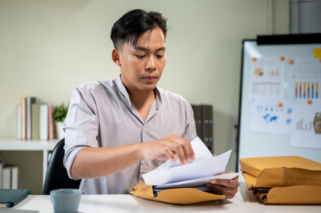 Asian businessman office worker looking at documents taking out from envelope aside coffee on table....