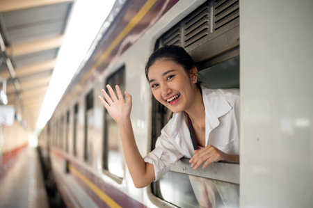 Asian woman smiling as leaning head and waving a hand out of carriage's window at train station...
