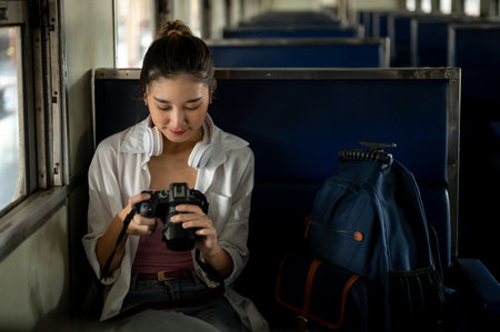 Pretty asian woman sitting on carriage bench and holding camera looking at photos taken at train...