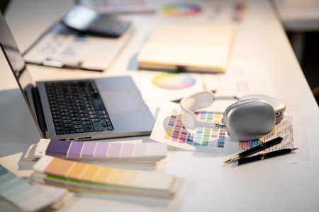 Laptop with headphones and pens placing atop color charts or palette on working table in designer's...