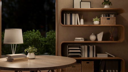 Books and lamp on round wooden table with display shelf in a dim lit living room or bedroom at...