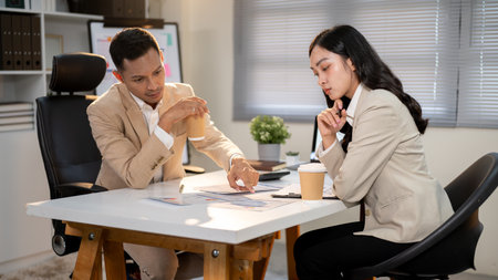 Businessman or office worker pointing a finger in document to a woman coworker at working table....