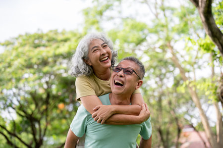 Glasses old man carrying old woman on his back as laughing together while standing or walking in park. Elderly couple, Green Nature, Chilling Outdoor.の写真素材
