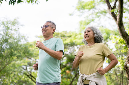 Glasses old man and old woman smiling while running or jogging together inside the public park. Elderly couple, Green Nature, Chilling Outdoor.の写真素材