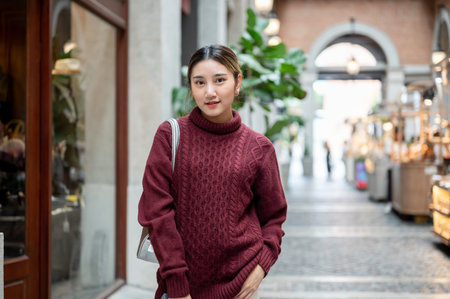 Young asian woman in knit sweater with bag standing and posing in a hallway of shopping mall or market. Travel tourist, Autumn cloth.の写真素材