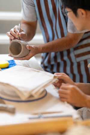 Pottery teacher holding brush showing how to add texture on clay mug on work table in class or...