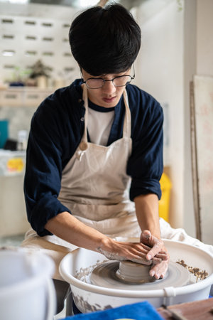 Young man pottery artist molding clay into a bowl on spinning throwing wheel in a class or studio....