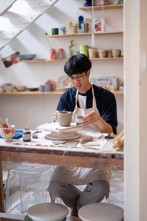 Pottery artist holding handle to a clay mug on throwing wheel at working table in a class or studio....