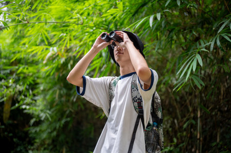 Backpacker tourist man holding binoculars looking at wild bird on a solo hiking or trekking in the...