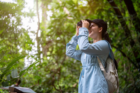 Pretty asian woman tourist smiling while looking through binoculars during a hiking or trekking in...