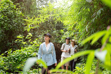 Woman tourist walking in front of man and friend while holding a cane during forest hiking or...