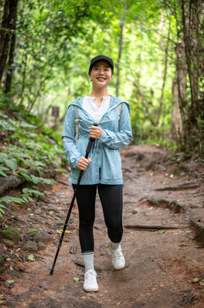 Pretty asian tourist woman looking ahead and walking downhill holding trekking cane on a hiking in...