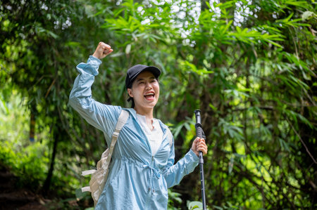Happy asian tourist woman standing holding trekking cane and raising her fist on a solo hiking in...