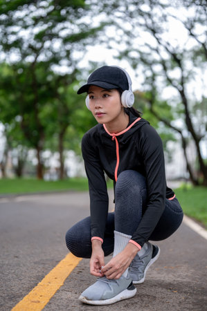 Young woman in sportswear and headphone tying her shoelace before exercise or workout in the park....