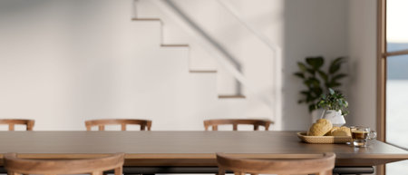 Breads and coffee cup on wooden dining table and chairs beside stairs in modern house or office...