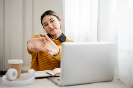Asian woman student or a writer stretching hands while looking at laptop aside coffee on table. Work...