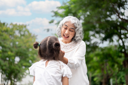 Old woman grandmother holding or hands cupping face of kid girl granddaughter in a park or garden. Child development, Public space, Outdoor Activity.の写真素材