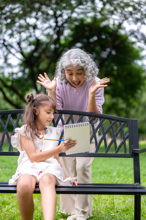 Old woman granny making funny face while looking at notebook that a kid girl granddaughter showing. Child development, Public space, Outdoor Activity.の写真素材