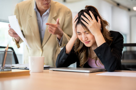 Asian businesswoman holding head in pain or stressed while getting scolded by boss at office's table. Meeting room, Corporate jobs, Modern company.の写真素材