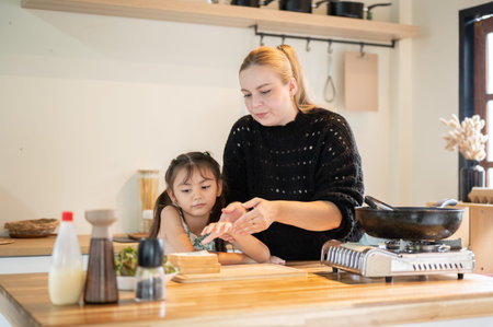 Caucasian white mother teaching asian kid daughter how to make sandwich at kitchen cooking counter....