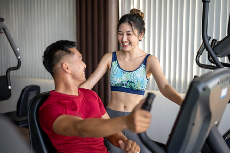 Pretty asian woman client smiling at a fitness trainer man teaching on exercise equipment in the...
