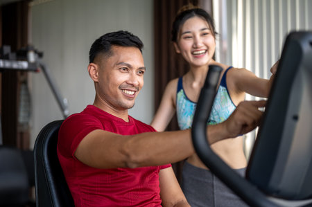 Smiling fitness trainer man teaching pretty asian woman client how to use exercise equipment in gym....
