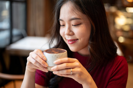 Pretty young asian woman holding and smelling tiramisu cup with both hand while sitting in a cafe. Sweet Dessert, Aesthetic Cafe, Shop Recommendation.の写真素材